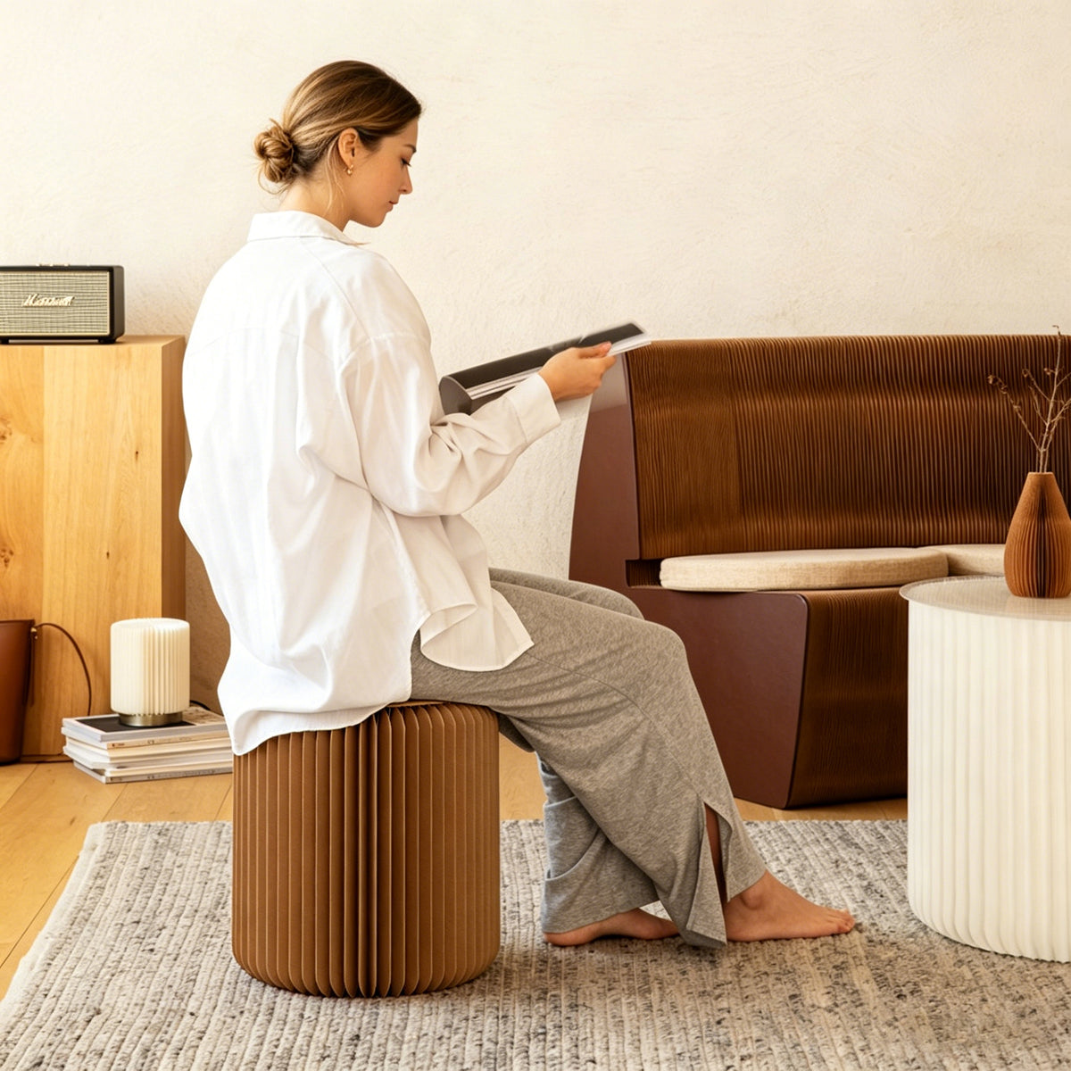Woman seated on brown honeycomb paper stool in modern living room reading a magazine