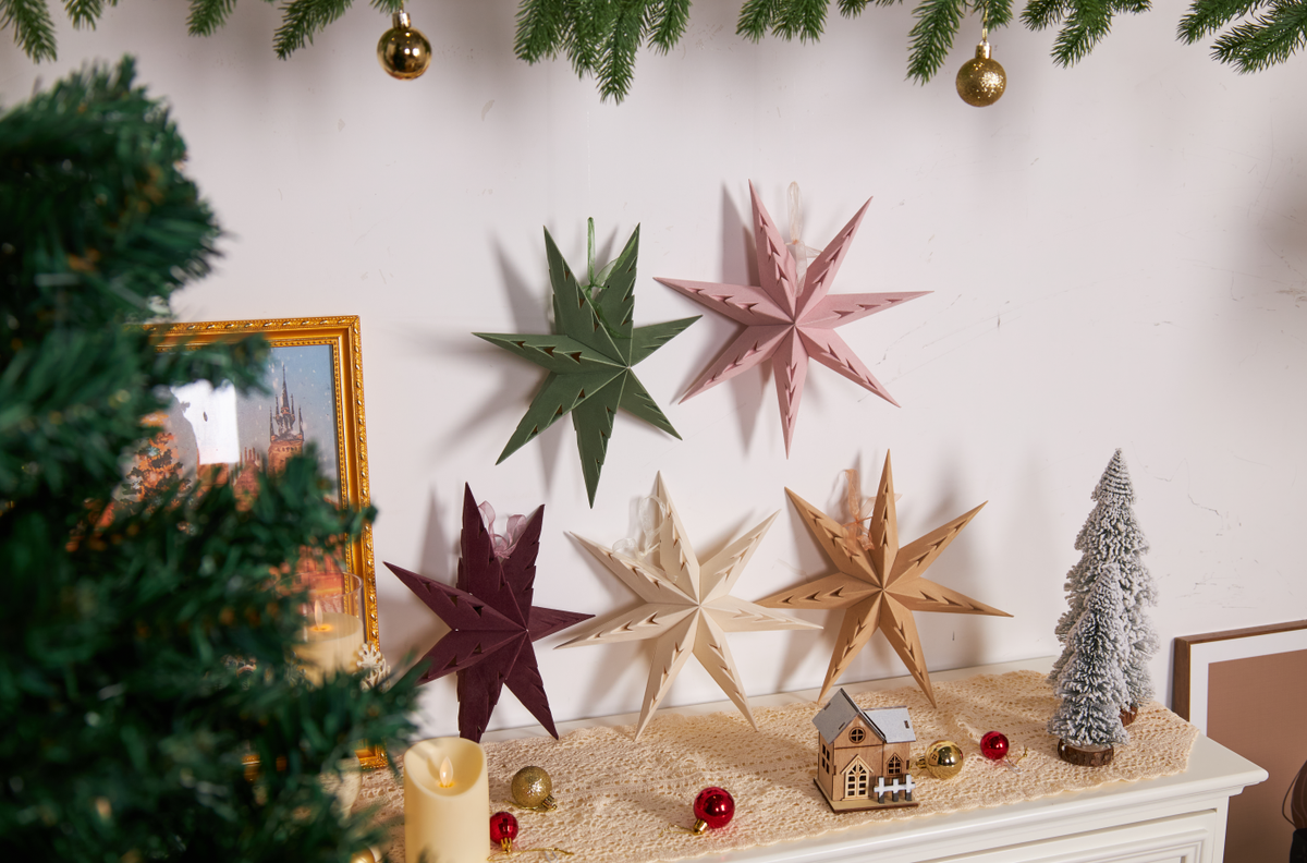 Assorted paper star decorations in green pink cream and gold on white wall with Christmas mantel display – strengthening Christmas assortments
