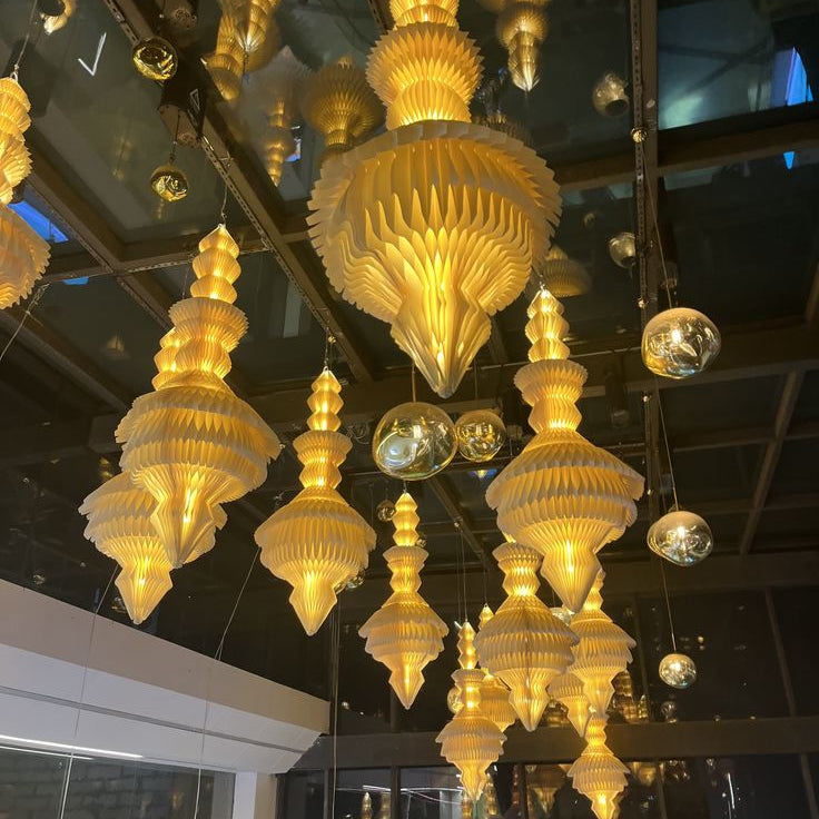 Cluster of illuminated gold honeycomb paper pendant lampshades hanging in retail display setting