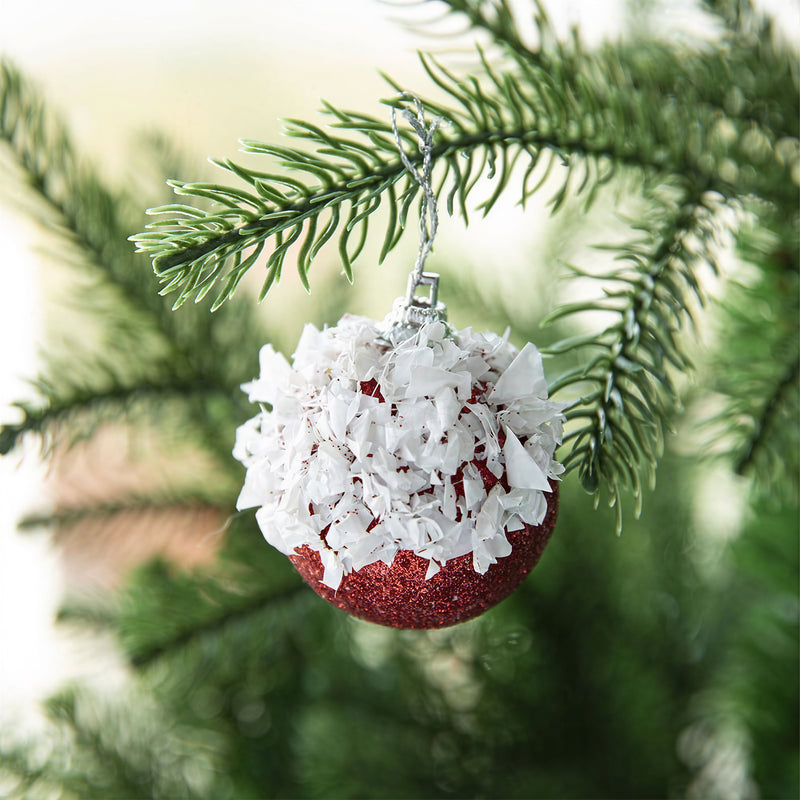 Red and white honeycomb paper ornament hanging from a Christmas tree branch