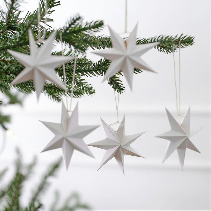 White paper star ornaments hanging from evergreen branches